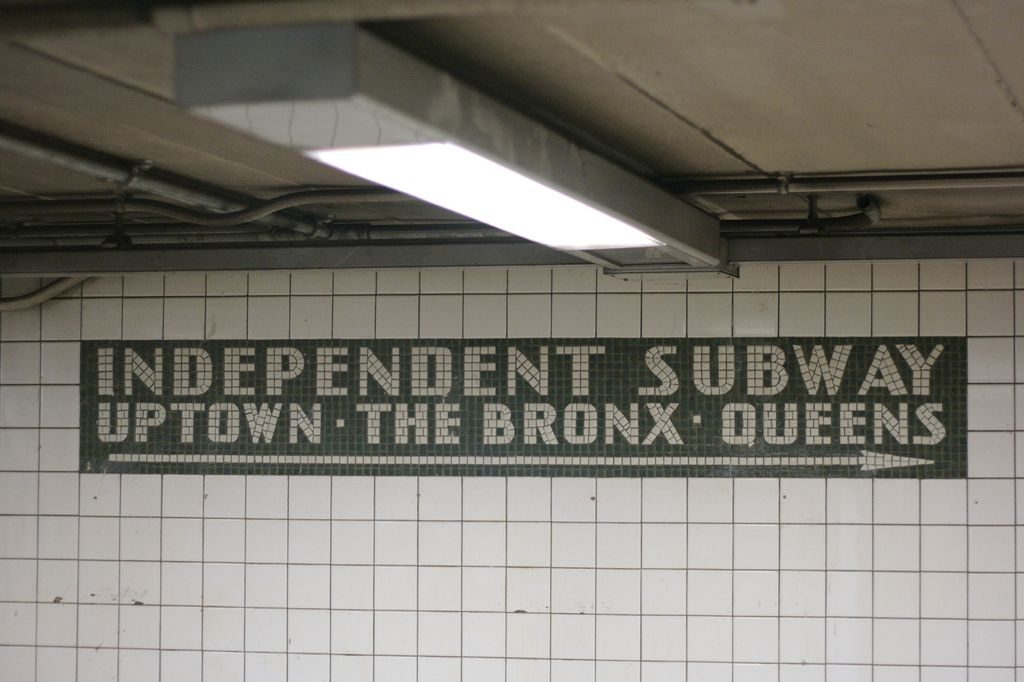 New York City subway station sign in Helvetica on a tile-mounted panel — the Unimark International wayfinding system